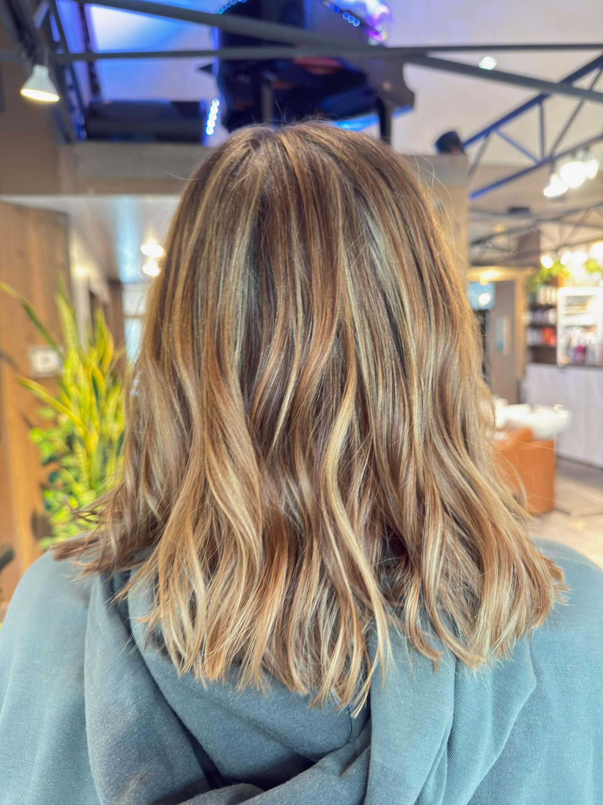 Woman with wavy, highlighted hair in a salon setting.