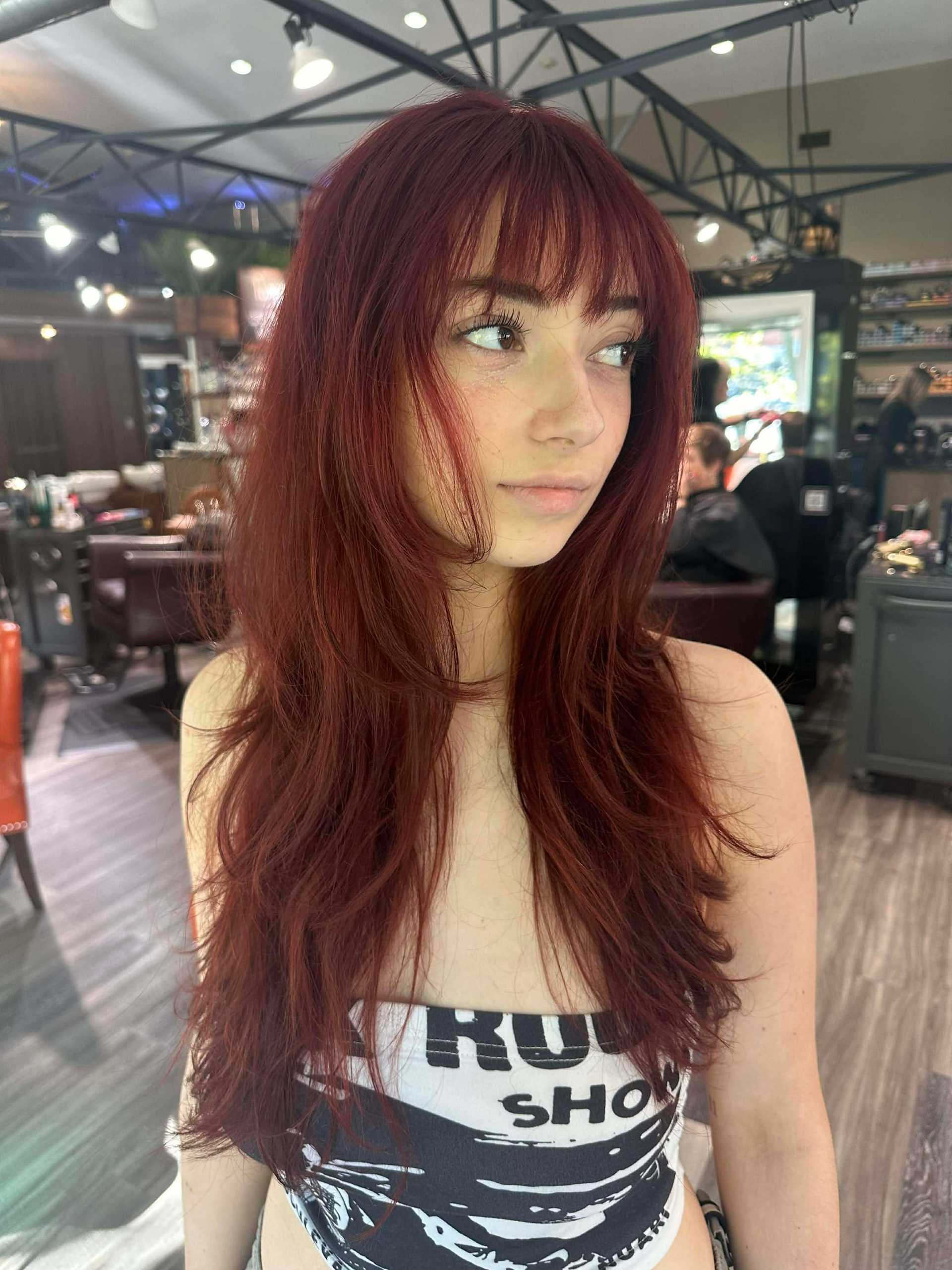 Woman with long red hair in a salon, wearing a printed crop top.