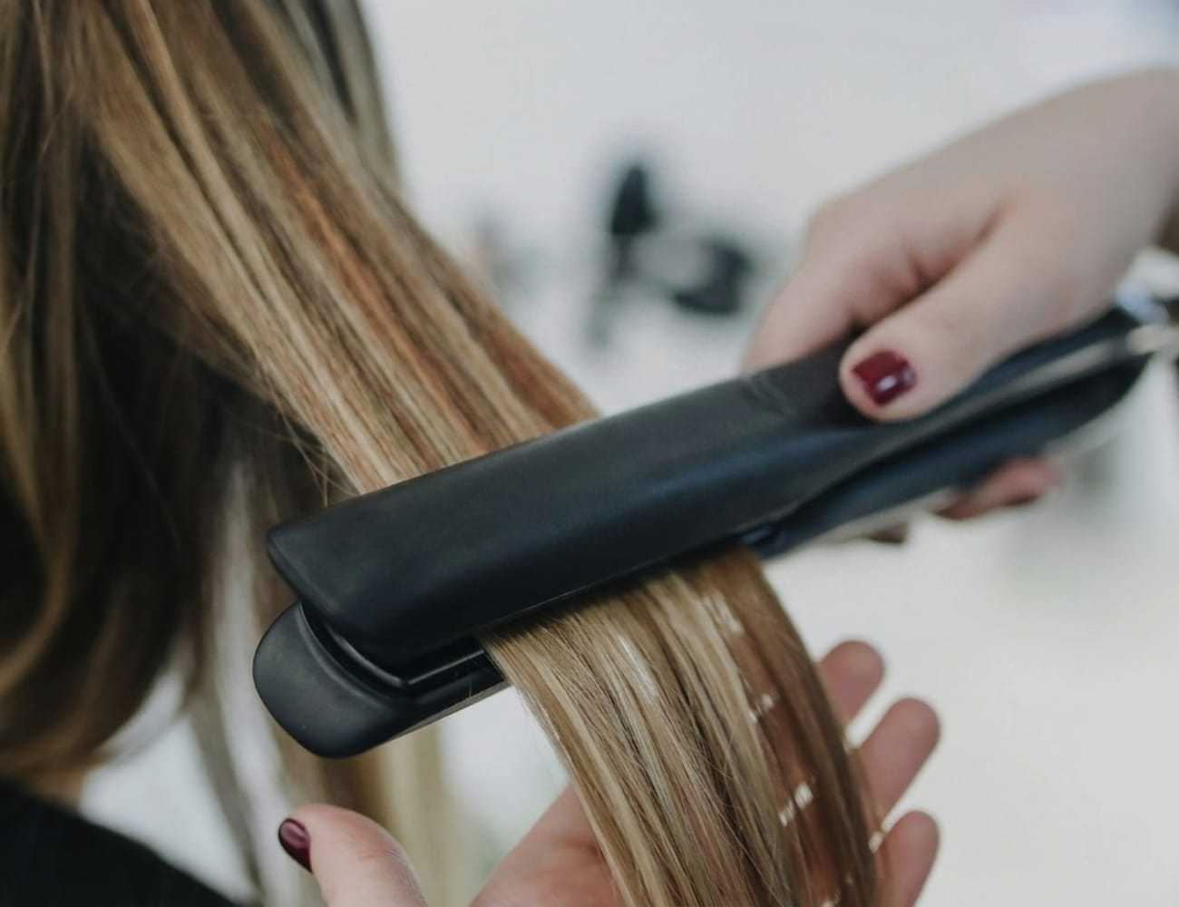 Hair being straightened with a flat iron, close-up view.