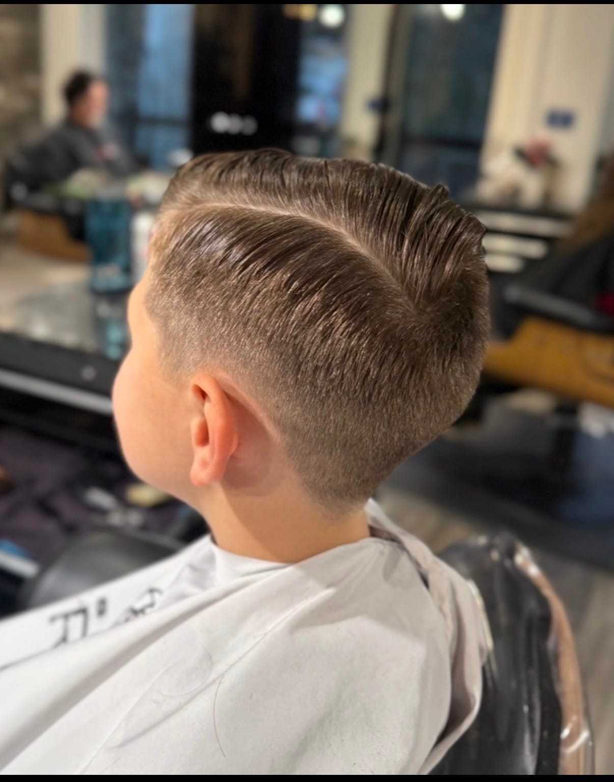 Boy with slicked-back haircut sitting in a salon chair.
